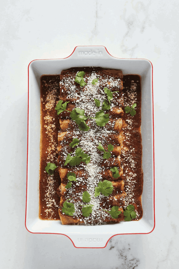 A baking dish full of enchiladas with sauce