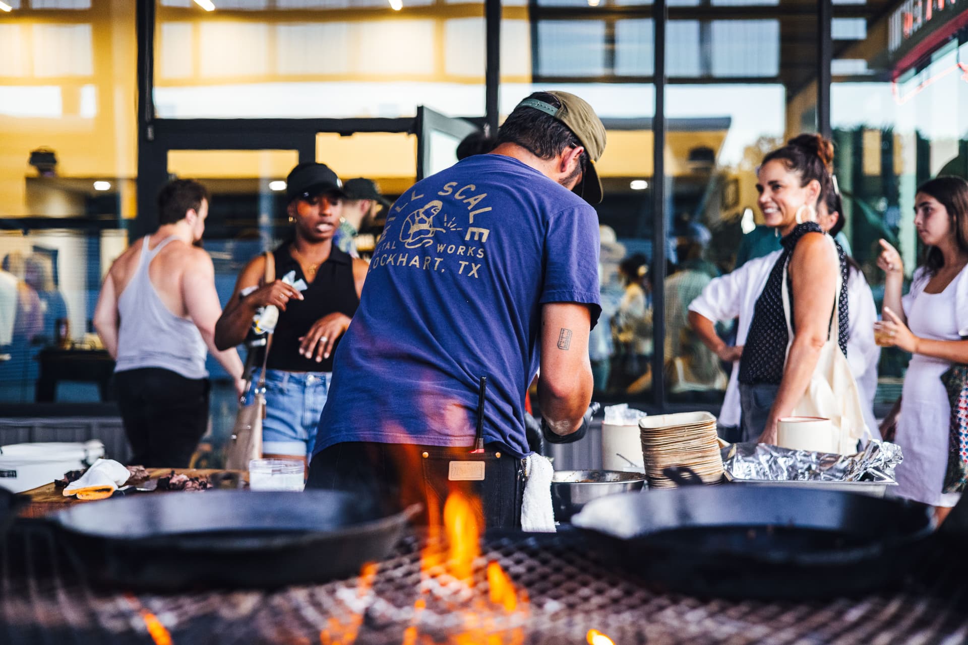 A pitmaster cooks over an open fire for customers
